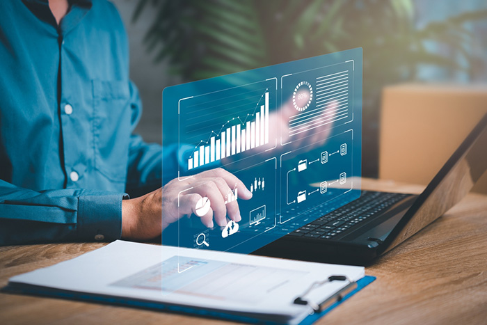 Person analyzing data on laptop with futuristic digital dashboard displaying charts and analytics.